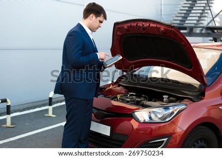Portrait of sales manager making photo under car bonnet