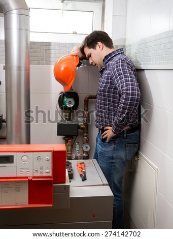 Plumber with red hard hat looking at complicated heating system
