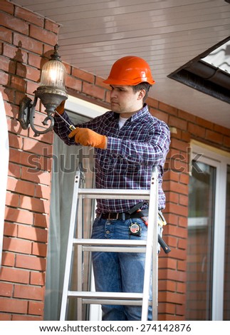Professional electrician standing on ladder and changing outdoor lamp