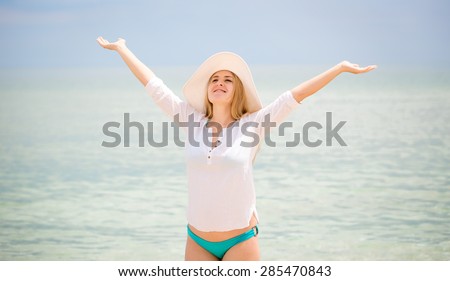 Portrait of happy woman in white shirt and hat stretching at sea