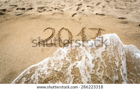 Closeup shot of 2017 written on sand being washed off by wave