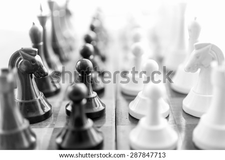 Black and white closeup photo of chess pieces standing in rows face to face