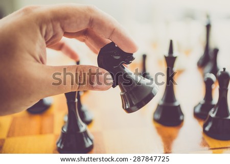 Closeup toned photo of man making move with black horse at chess game