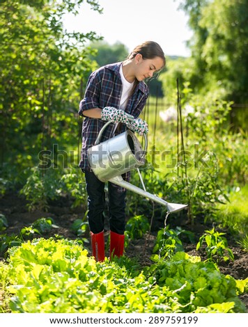 Cute little girl watering plants in garden at hot sunny day