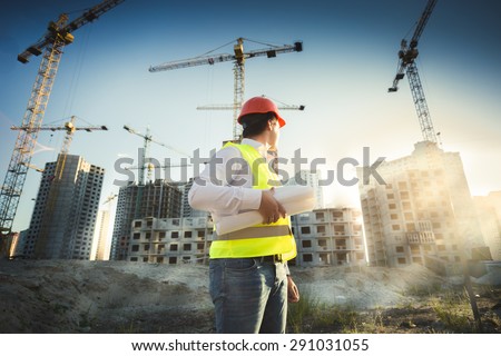 Man in hardhat and green jacket posing on building site at sunset