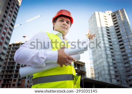 Closeup portrait of foreman in helmet showing building site under construction