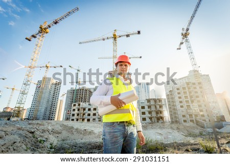 Portrait of construction inspector posing with blueprints on building site