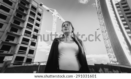 Closeup black and white portrait of frustrated and depressed woman posing against skyscrapers under construction