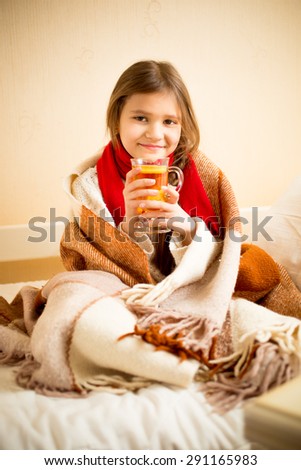 Portrait of cute girl covered in blanket drinking hot tea with lemon in bed