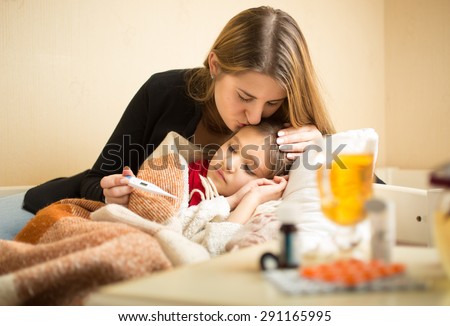 Portrait of young caring mother kissing sick daughter in head