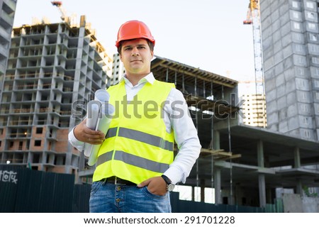 Portrait of site manager posing with blueprints against unfinished building