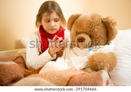Portrait of cute girl playing and measuring teddy\'s bear temperature with thermometer