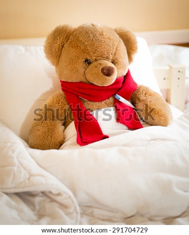 Closeup photo of teddy bear in red scarf lying in bed