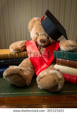 Closeup photo of brown teddy bear wearing graduation cap leaning on books