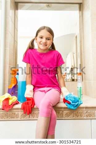 Portrait of smiling girl sitting on sink at bathroom while doing cleaning