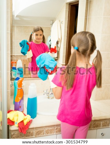 Portrait of cute girl cleaning and polishing mirror at bathroom