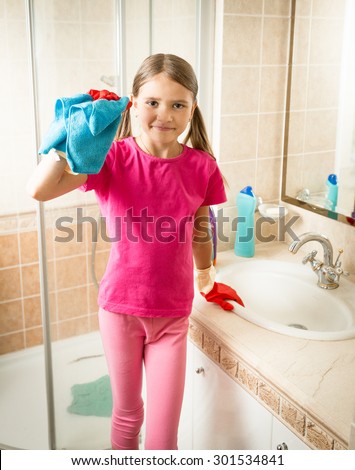Brunette girl posing with blue cloth while cleaning sink at bathroom