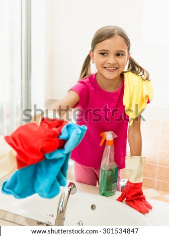 Funny smiling girl polishing mirror at bathroom while cleaning house