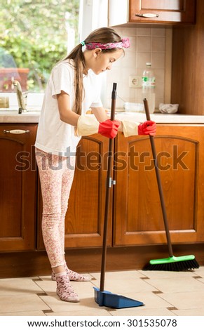 Little brunette girl cleaning floor on kitchen with broom and scoop
