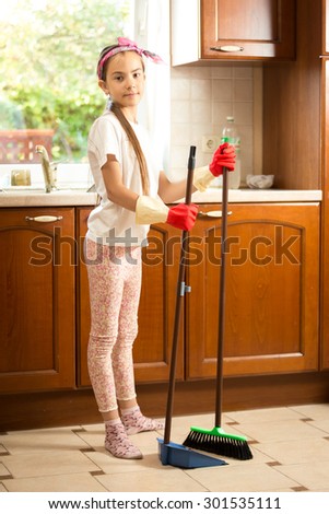 Cute girl in rubber gloves sweeping floor at kitchen with swab and scoop