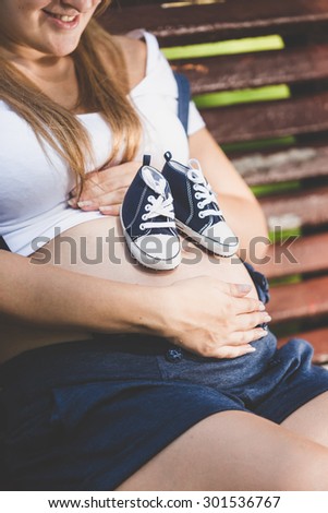 Toned closeup photo of baby shoes on female pregnant abdomen
