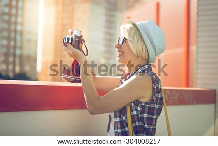 Toned portrait of smiling hipster girl making photo on film camera