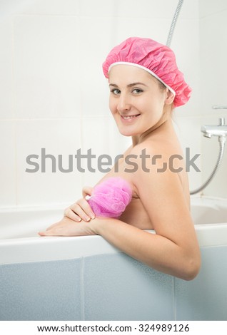 Portrait of beautiful smiling woman in shower cap sitting in bath
