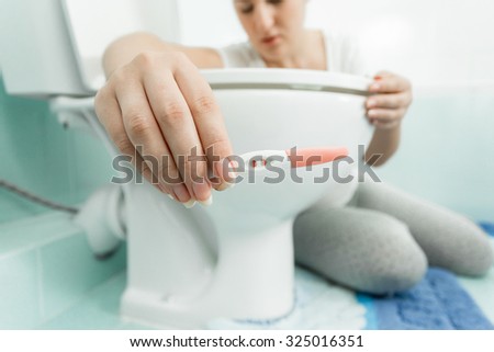 Closeup portrait of woman sitting on floor at bathroom and holding positive pregnancy test