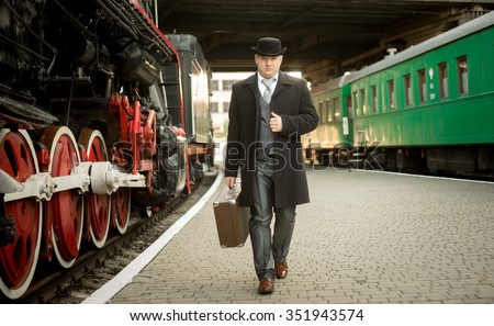 Handsome man in retro suit with suitcase walking on the train platform