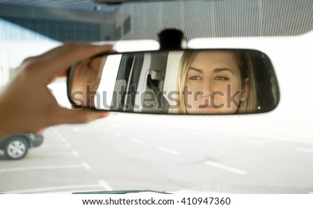 Closeup photo of woman adjusting car mirror and looking in the reflection