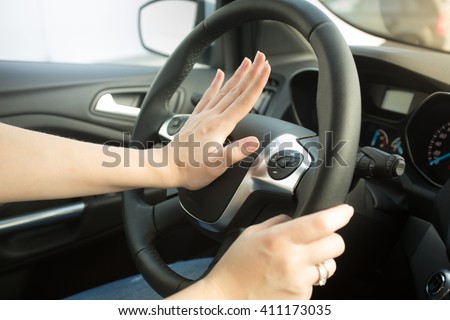 Closeup photo of annoyed woman driving car and honking