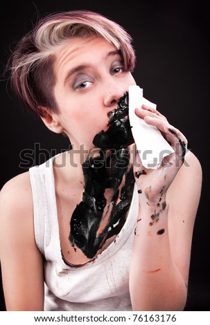 Young caucasian lady covered in black substance and cleaning with napkin