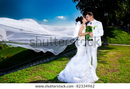  Young newly married couple posing in parkwind lifting long bridal veil