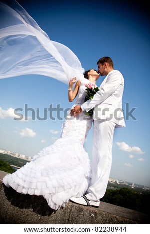 newly married couple kissing.wind lifting long white bridal veil