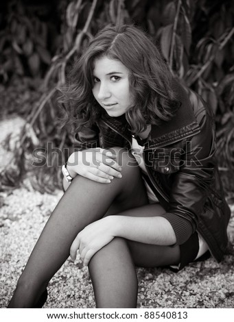 black and white photo of cute caucasian girl sitting on ground touching legs