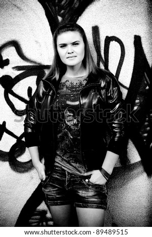 Black and white photo of beautiful girl posing near graffiti wall