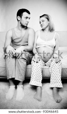 Black and white photo of young man sitting on couch with his pregnant wife