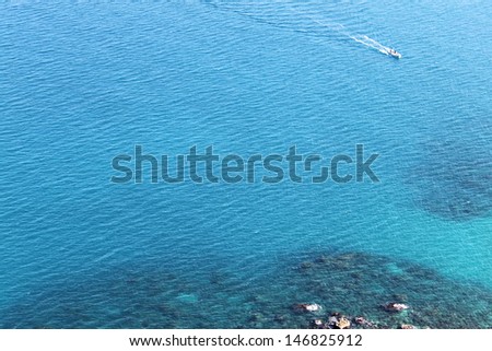 A motor boat going towards the coastline in turquoise wavy waters.
