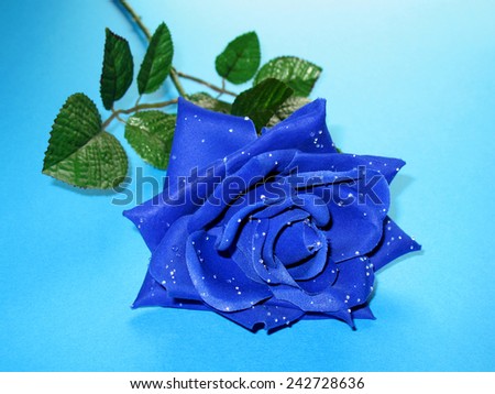 An artificial blue rose with dewy petals on a blue background.
