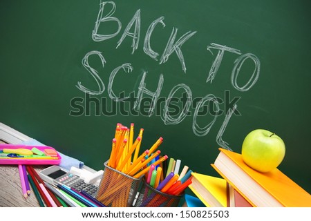 Back to school. An apple, books and school accessories against a school board.