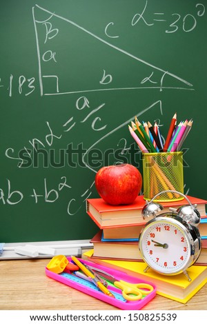 Back to school. An alarm clock, books and school accessories against a school board (mathematical formulas).