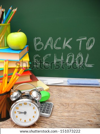 Alarm clock and school accessories against a school board. Back to school.