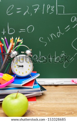 Apple, alarm clock and other school subjects against a school board (mathematical formulas).