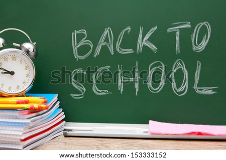 Back to school. An alarm clock, writing-books and pencils against a school board.