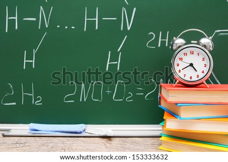 Alarm clock on books. Against a school board with chemical formulas.