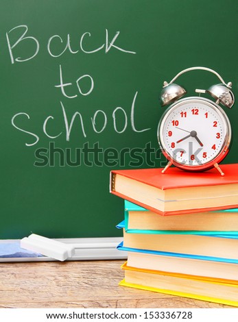 Back to school. An alarm clock on a pile of books against a school board.
