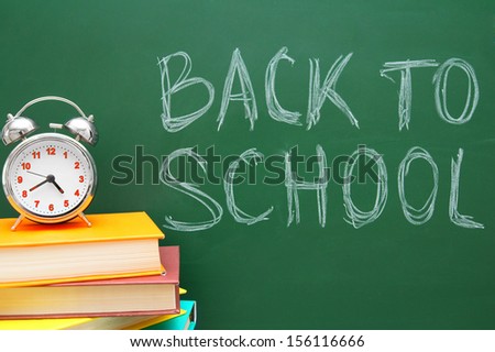 Back to school. An alarm clock and books against a school board.