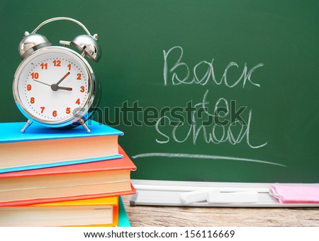 Alarm clock and books against a school board. Back to school.