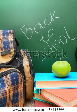 Back to school. School bag, apple and books against a school board.