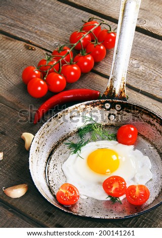 Fried egg, fennel and tomatoes in an old frying pan. Fresh tomatoes, hot pepper and garlic. On a wooden background.